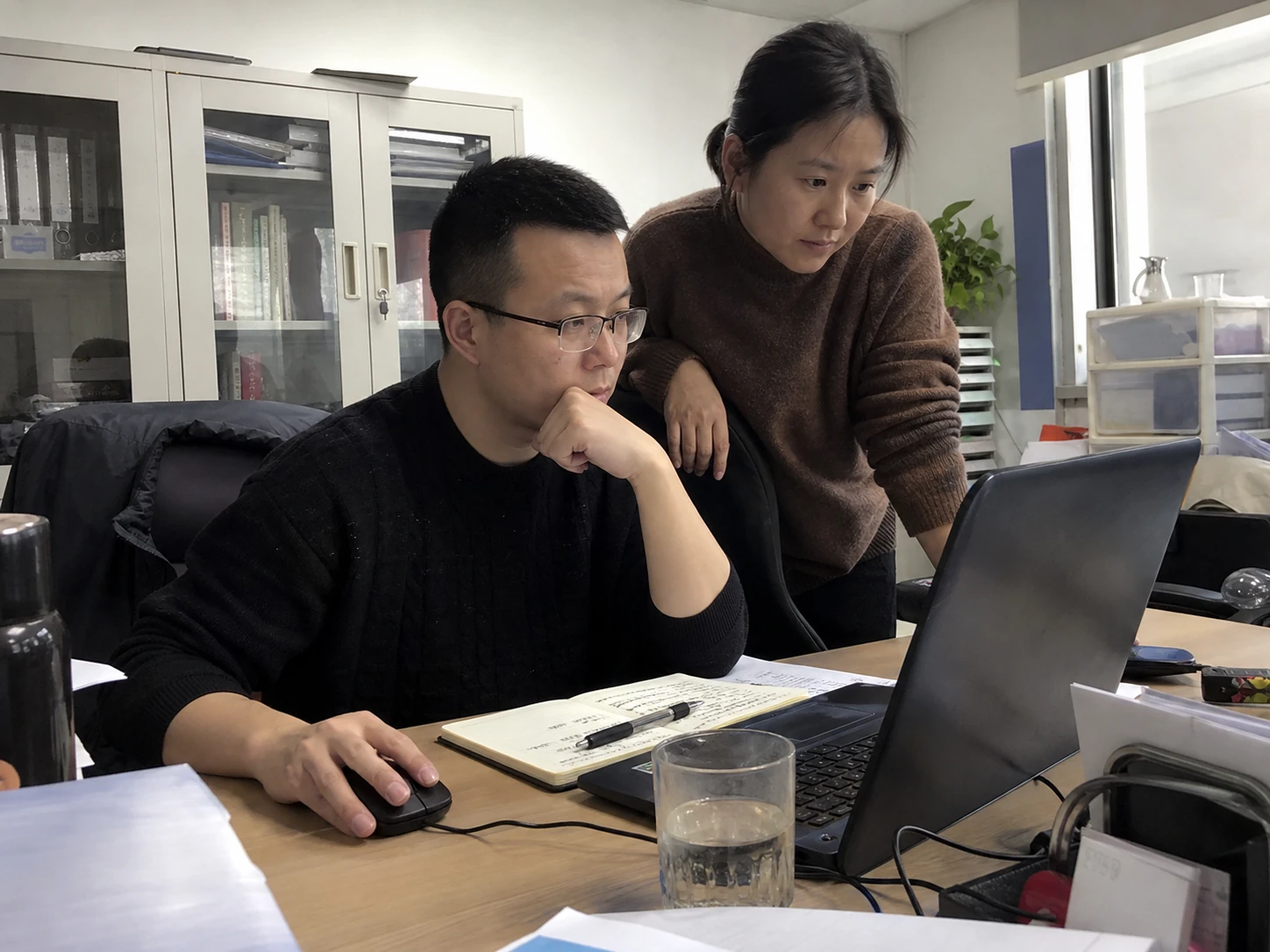 两位同事在办公桌旁核对记录与下一步任务