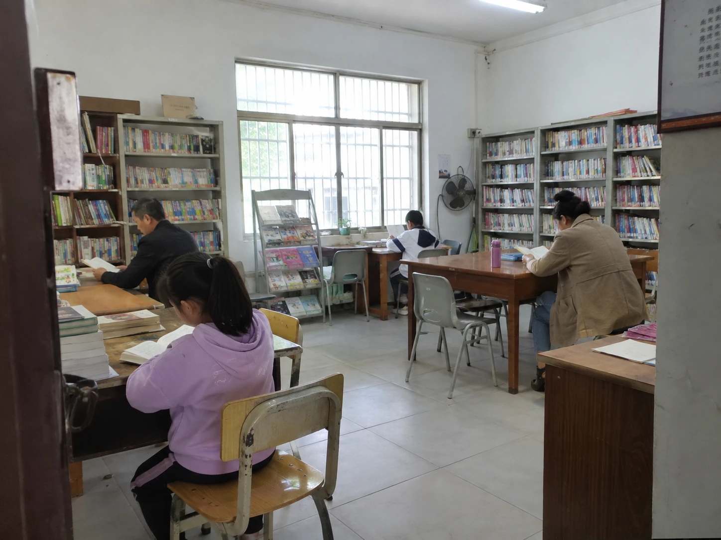 社区阅读室里的书架、普通桌椅和安静阅读的人们
